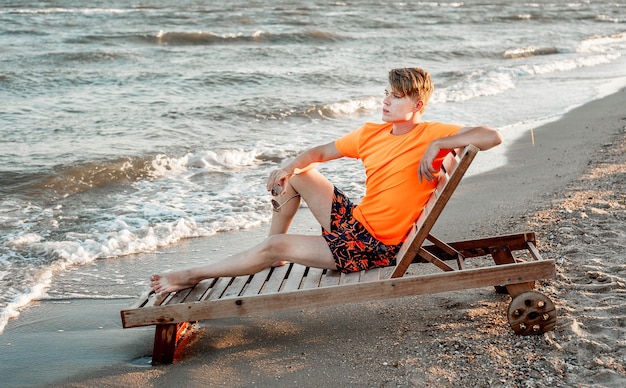Un ragazzo in maglietta e pantaloncini si siede su un lettino in riva al mare