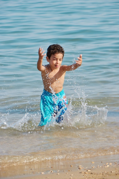 Un ragazzo in pantaloncini blu salta in acqua in spiaggia.