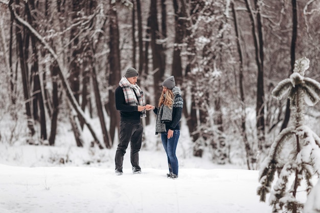Un ragazzo inginocchiato mette un anello di fidanzamento sulla mano di una ragazza, facendo una proposta per sposarsi in inverno in una foresta innevata