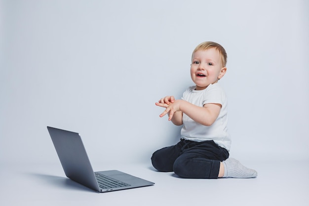 Un ragazzo intelligente di 34 anni si siede con un laptop su sfondo bianco Un bambino con una maglietta bianca e pantaloni neri si siede davanti a un laptop e guarda la telecamera Bambini moderni