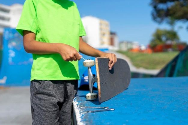 Un ragazzo irriconoscibile ripara la ruota del suo skateboard dopo averlo usato all'interno del parco degli skateboarder