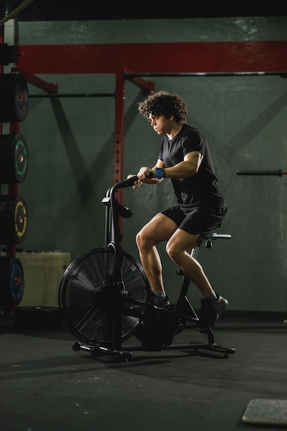 Un ragazzo muscoloso sta facendo un duro allenamento di crossfit in bici in palestra.