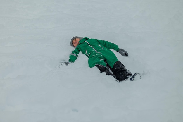 Un ragazzo nella neve fa un angelo della neve il ragazzo gioca fuori un bambino nella neve giochi all'aperto