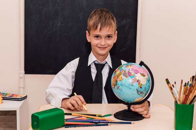 Un ragazzo siede a un banco di scuola a una lezione di geografia