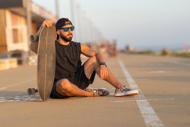 Un ragazzo simpatico seduto su una strada con uno skateboard