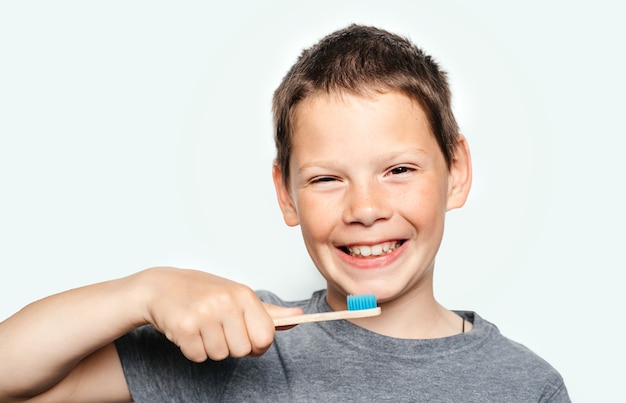 Un ragazzo sorridente che tiene in mano uno spazzolino da denti ecologico in bambù e mostra i denti