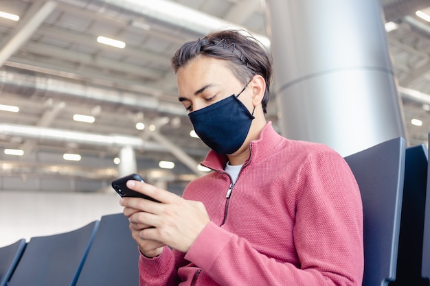 Un ragazzo sta aspettando un volo con una maschera medica sul viso nella lounge dell'aeroporto.