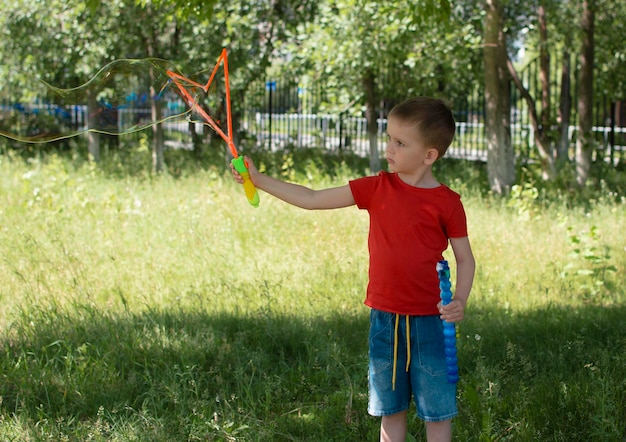 Un ragazzo sta giocando con enormi bolle di sapone nel parco Vacanze estive stile di vita attivo Allegro bambino affascinante gode di un sano gioco estivo all'aperto