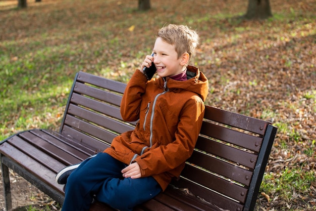 Un ragazzo sta parlando al telefono e ridendo mentre è seduto su una panchina del parco in autunno