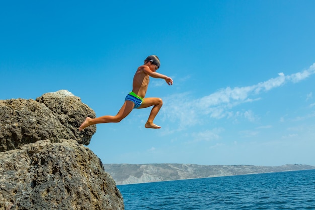 Un ragazzo sta saltando dalla scogliera in mare in una calda giornata estiva Vacanze sulla spiaggia Il concetto di turismo attivo e ricreazione