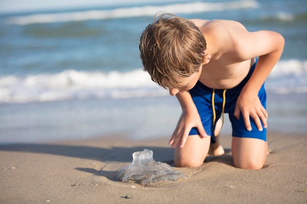 Un ragazzo vicino al mare esamina una medusa Bambino che riposa sulla spiaggia