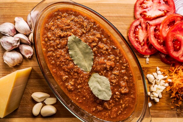 Un ragù alla bolognese fatto in casa con foglie di alloro in una grande ciotola di vetro con diversi tipi di verdure intorno