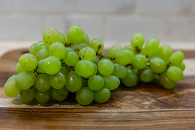 Un ramo di uva verde su un tagliere di legno in cucina Spuntino sano e vegetarianismo Primo piano