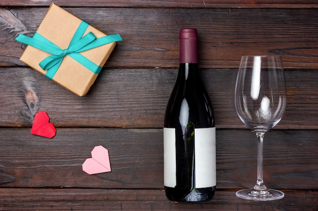 Un regalo avvolto in carta artigianale, una bottiglia di vino e un bicchiere di vino su un tavolo di legno scuro. Vista dall'alto.