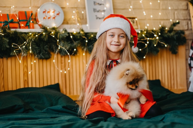 Un regalo di benvenuto per Natale un cucciolo di Pomerania. Una bambina carina ha ricevuto un cucciolo come regalo per Natale. La gioia del dono. Bambino felice.