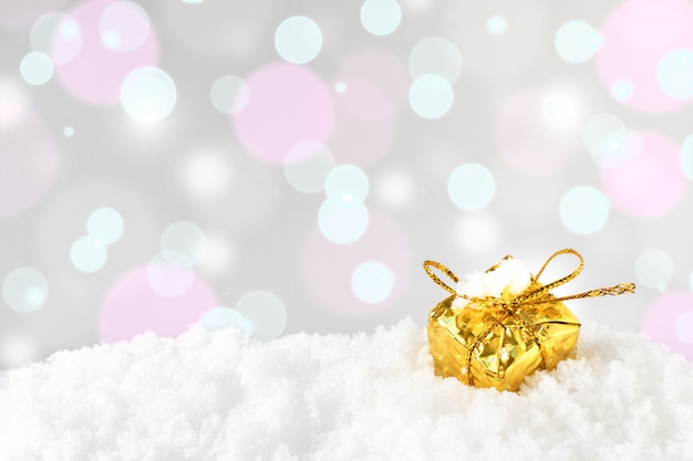 Un regalo di Natale o Capodanno decorativo lucido dorato con un arco è in piedi nella neve sullo sfondo