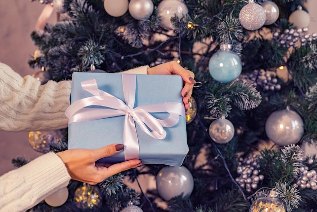 Un regalo nelle mani della donna sullo sfondo delle luci dell'albero di Natale