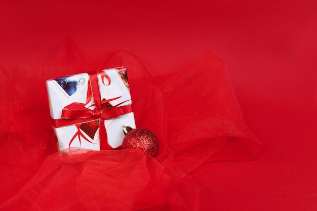 Un regalo per il nuovo anno e una palla di Natale su un albero di Natale su sfondo rosso. Biglietto natalizio