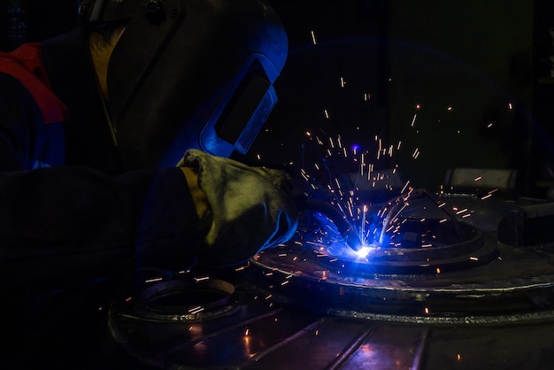 Un riflesso lente durante la saldatura elettrica semiautomatica manuale con scintille lavoratore industriale professionista in maschera protettiva nera