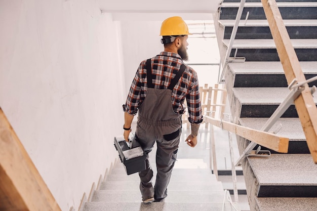 Un riparatore che scende le scale in un edificio in costruzione con la cassetta degli attrezzi in mano