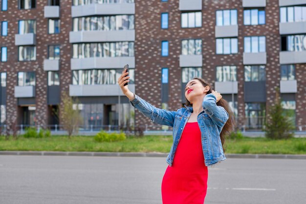 Un ritratto alla moda di una bella ragazza in un elegante vestito rosso - con un telefono in città