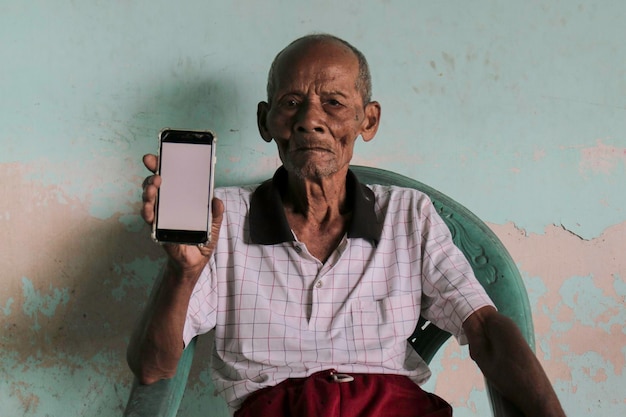 Un ritratto del vecchio nonno indonesiano che mostra lo smartphone con schermo bianco