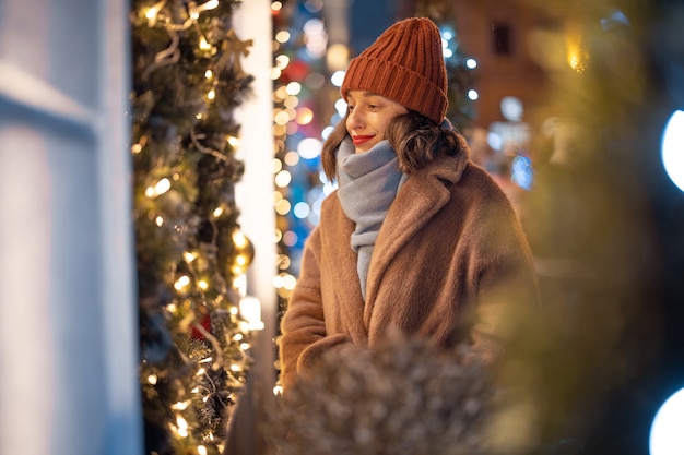 Un ritratto di bella donna che guarda la vetrina decorata di Natale, camminando nel centro cittadino durante le vacanze invernali, alla ricerca di regali per le vacanze. Foto di alta qualità