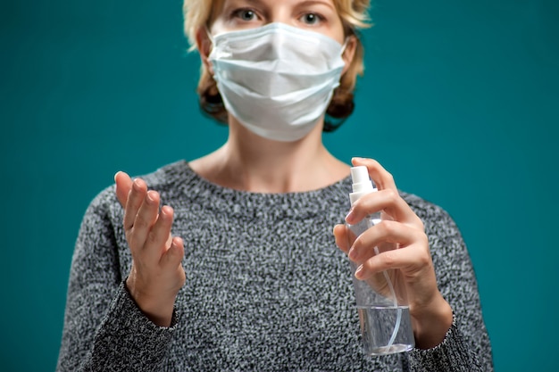 Un ritratto di donna con mascherina medica applicando spray disinfettante sulle mani. Concetto di persone, medicina e assistenza sanitaria. Protezione dal coronavirus