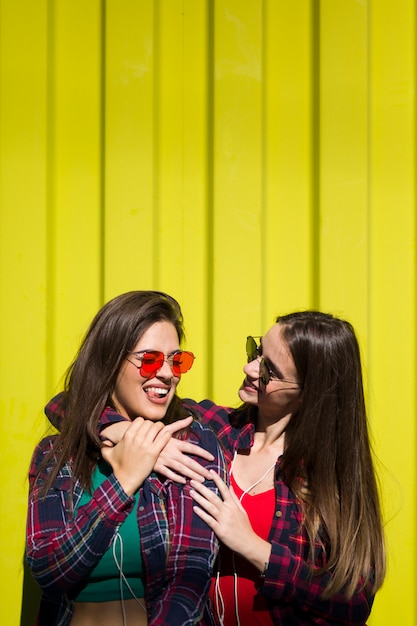 Un ritratto di due giovani amici felici delle donne che stanno all'aperto sopra la parete gialla