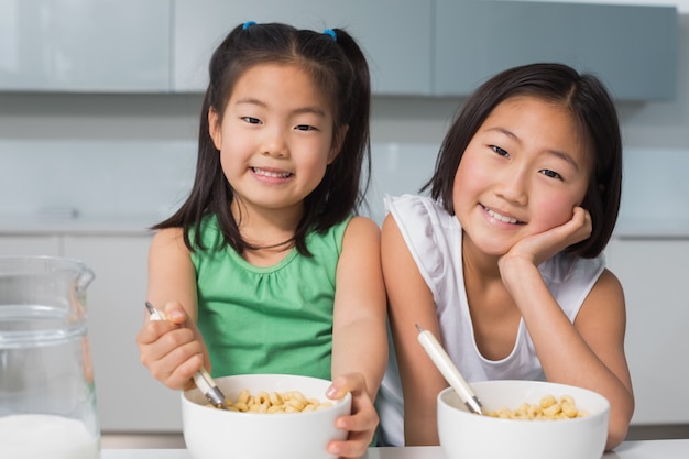 Un ritratto di due ragazze sorridenti che si siedono con le ciotole in cucina