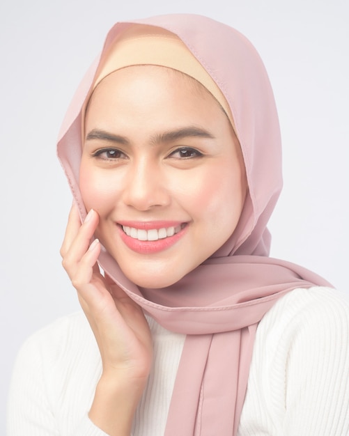 Un ritratto di giovane donna musulmana sorridente che indossa un hijab rosa su bianco.