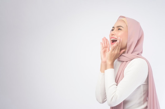 Un ritratto di giovane donna musulmana sorridente che indossa un hijab rosa su bianco.