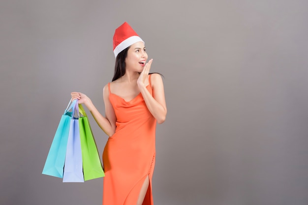 Un ritratto di giovane donna sorridente che indossa il cappello rosso di Babbo Natale è in possesso di borse della spesa