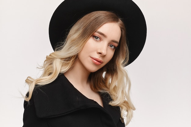 Un ritratto di moda di una giovane donna con trucco delicato e un cappello nero, isolato su sfondo bianco studio