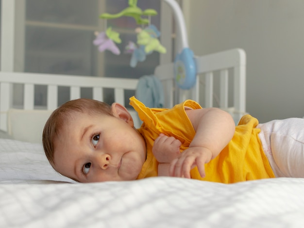 Un ritratto di un bambino felice faccia distesa sul letto, con una culla sfocata
