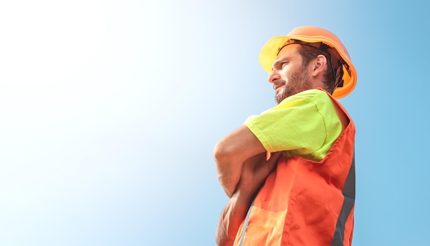 Un ritratto di un lavoratore si erge con fiducia in una tuta da lavoro arancione e un casco di sicurezza contro il cielo Concetto di lavoro industriale intelligente