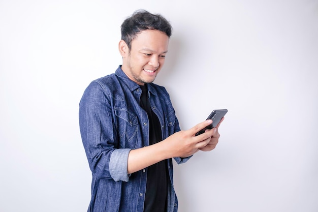 Un ritratto di un uomo asiatico sorridente sorride e tiene in mano il suo smartphone indossando una camicia blu navy isolata da uno sfondo bianco