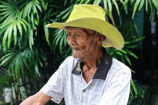 Un ritratto di un vecchio contadino indonesiano indossa un cappello giallo con una vecchia bicicletta