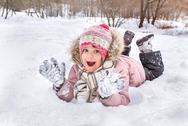 Un ritratto di una bambina felice sdraiata sulla neve che si gode il suo tempo