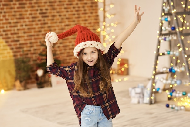 Un ritratto di una bambina in una casa di Natale decorato in un cappello di Natale