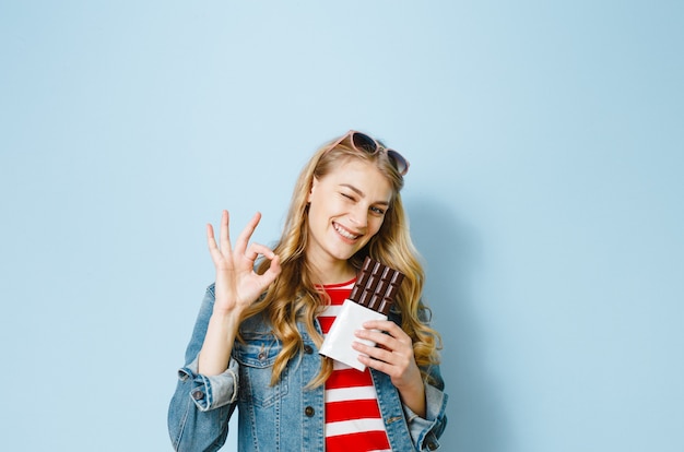 Un ritratto di una bella ragazza bionda che mangia cioccolato è eccitato su uno sfondo blu