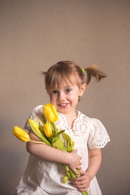 Un ritratto di una bellissima bambina con un mazzo di fiori di tulipani gialli