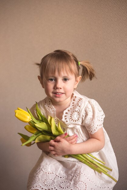 Un ritratto di una bellissima bambina con un mazzo di tulipani gialli