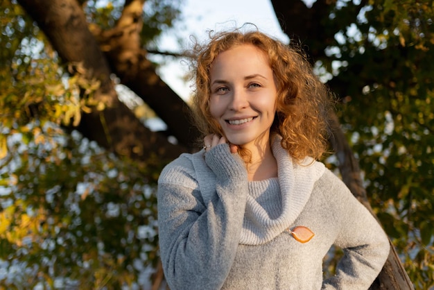 Un ritratto di una donna dai capelli rossi allegra in piedi nel parco in una giornata di primavera La ragazza sta guardando la telecamera e sorridente