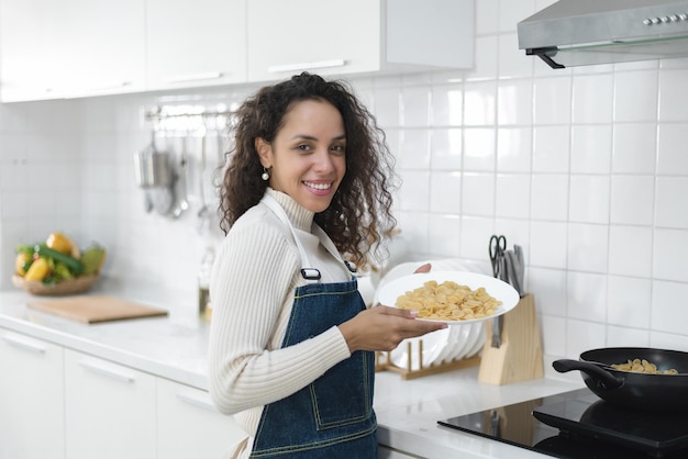 Un ritratto di una donna latina sorridente che si diverte a cucinare è in cucina