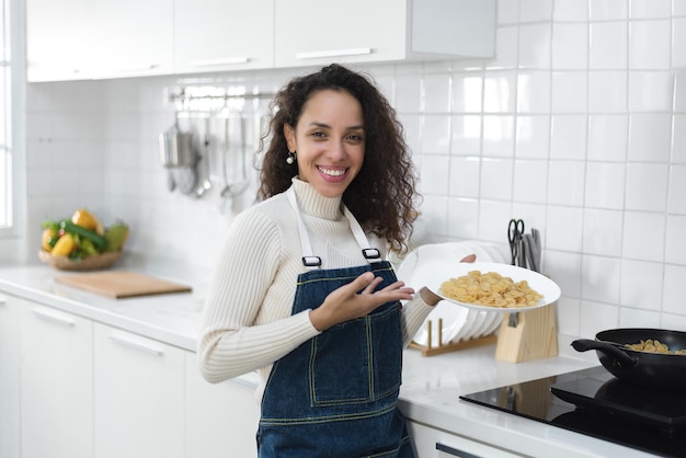 Un ritratto di una donna latina sorridente che si diverte a cucinare è in cucina