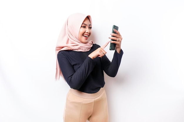 Un ritratto di una donna musulmana asiatica felice che indossa un hijab che tiene il suo telefono isolato da sfondo bianco