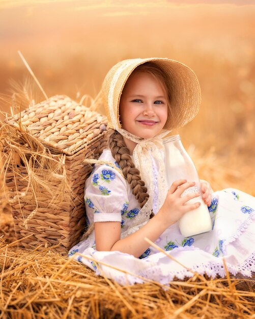 Un ritratto di una ragazza felice in un campo di grano al tramonto un bambino tiene un barattolo di vetro con latte contro