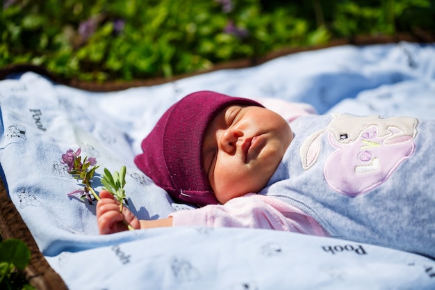 Un ritratto fotografico di un bambino con un berretto rosso giace su un plaid bianco sull'erba verde. La primavera è in strada, il sole splende sul bambino