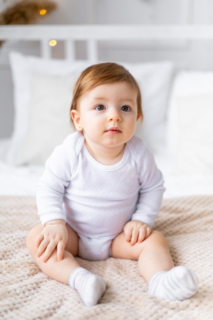 Un ritratto in primo piano di un bambino carino in una stanza luminosa in abiti bianchi a casa su un letto il concetto di beni per bambini